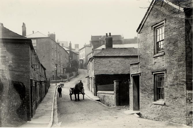 Duncombe street, Kingsbridge, looking west to fore street.   Man with wheelbarrow in background. Horses and cart coming down the hill.  Roger's Dairy on right behind low wall.  Cottages on left demolished and now site of fire station.