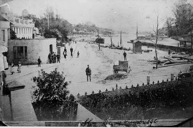 At the head of Kingsbridge estuary looking south from Ryeford House.   
A cart in road, logs lying all around estuary banks.