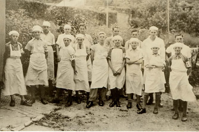 Milking class from Harry Rogers' farm at the bottom of Duncombe Street, Kingsbridge. 
Group of boys dressed in white aprons and caps, with numbered armbands.