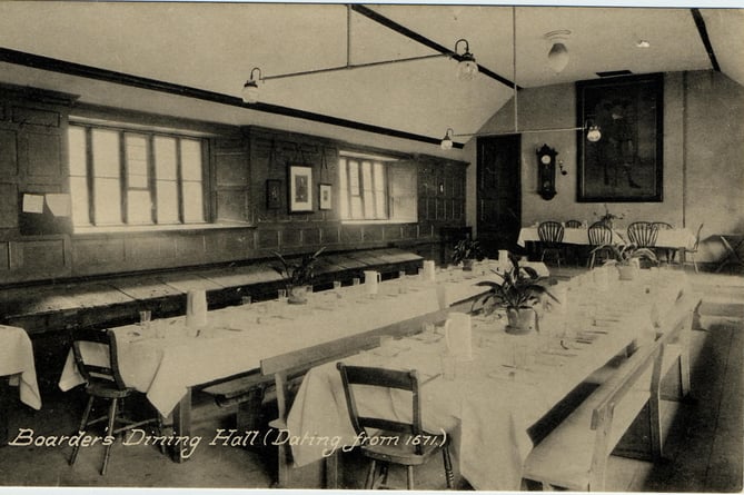 Kingsbridge Grammar School [KGS] - Boarders* dining hall dating from 1671.  Photo taken after 1933 when new school built.  Portrait in background is Dr. Crispin founder of school. Tables laid for a meal, gas lighting. 