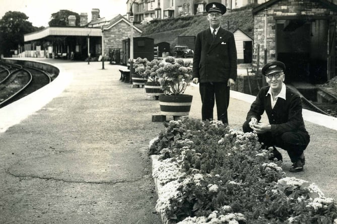 Two members of Staff on the platform at Kingsbridge Station. Tubs of flowers along the platform. 1960